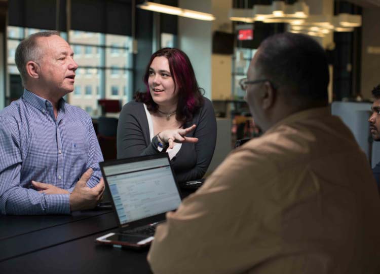 Three business professionals work together around a table with a computer